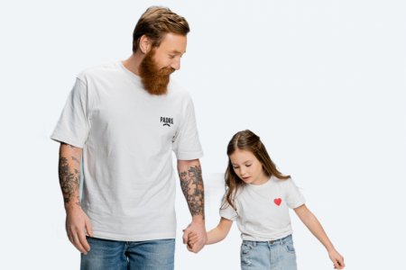 Un papa avec un t-shirt blanc avec écrit "Padre" au coeur tient la main de sa fille qui porte un t-shirt blanc avec un coeur rouge au coeur