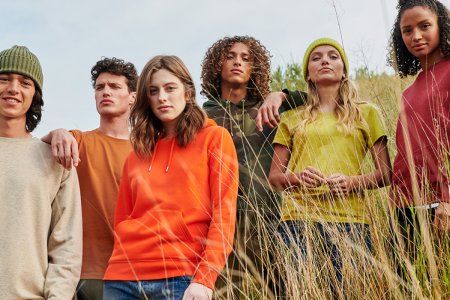 Six mannequins hommes et femmes posent dans sur une colline d'herbe en portant des sweats et t-shirts colorés de la marque Stanley/Stella
