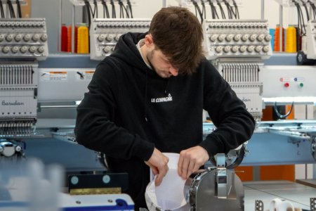 Un homme prépare une casquette blanche pour les machines de broderie 