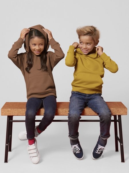 Deux enfants assis sur un banc portent des sweats à capuche Mini Cruiser en coloris Caramel et Ochre